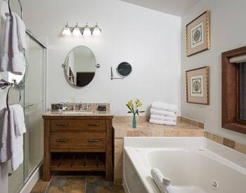 Wooden vainity with a marble top, jetted tub and fluffy white towels on the side of the tup. Window over the tub looking at the mountains.